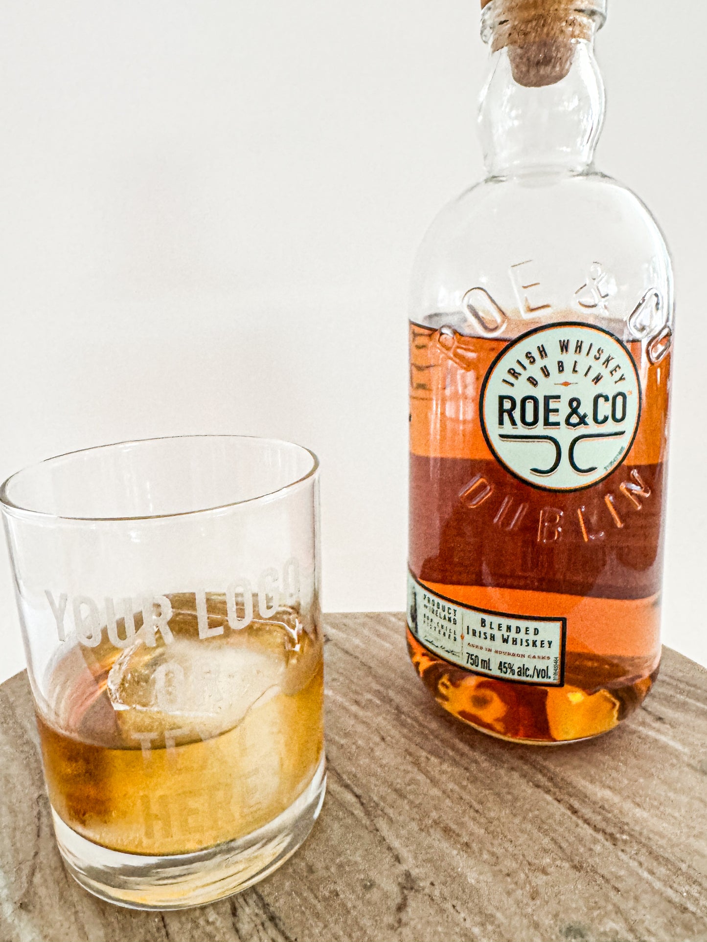 Bottle of Roe & Co Dublin whiskey and a glass with whiskey on a wooden surface.