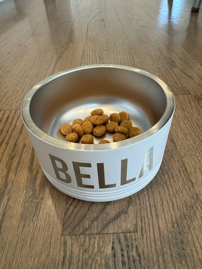 Stainless steel pet bowl with 'BELLA' on a wooden floor