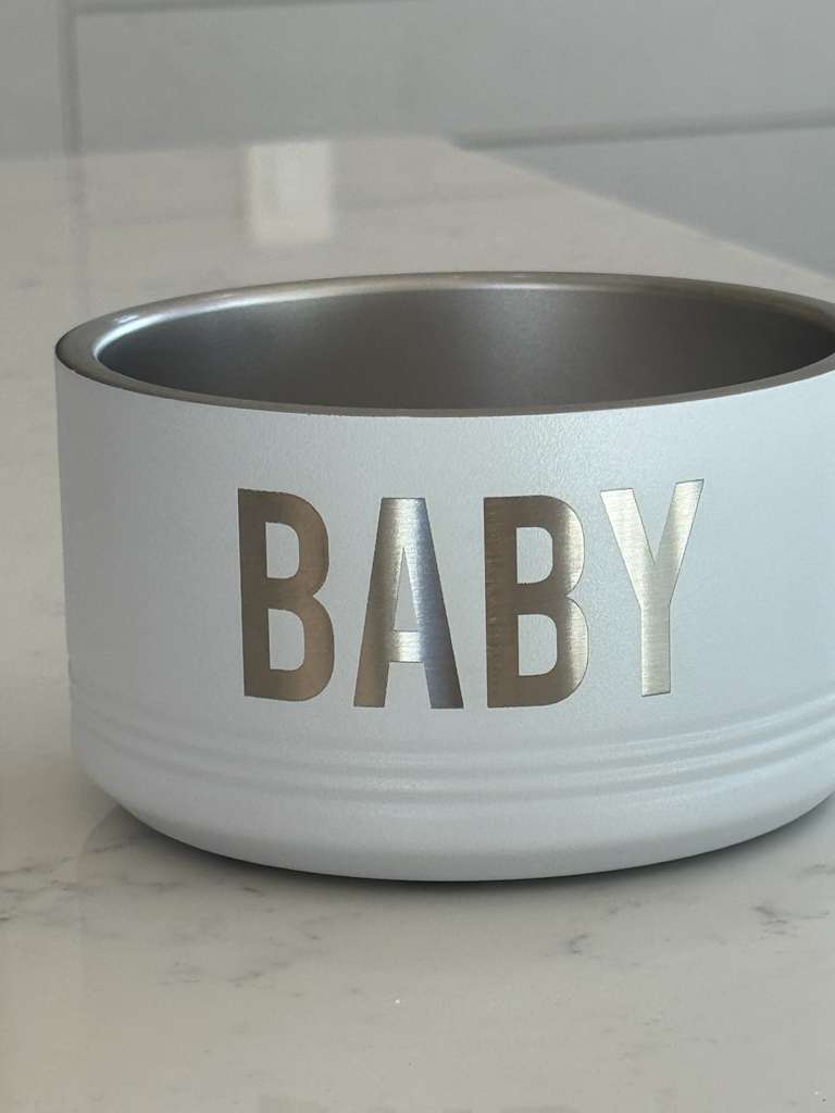 White pet bowl with 'BABY' printed on it on a marble surface.