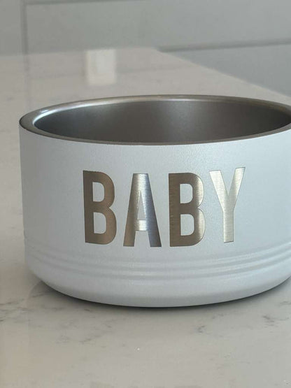 White pet bowl with 'BABY' printed on it on a marble surface.