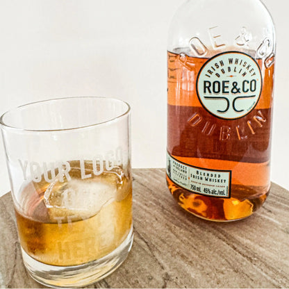Bottle of Roe & Co Dublin whiskey and a glass with whiskey on a wooden surface.